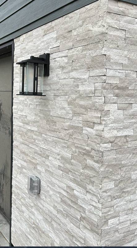 Black exterior wall light and weatherproof receptacle on a stacked stone wall