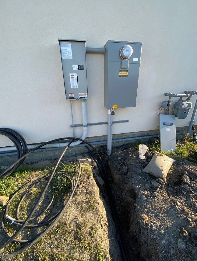 Meter base and outdoor disconnect on a stucco wall with underground cable laid beside an open trench