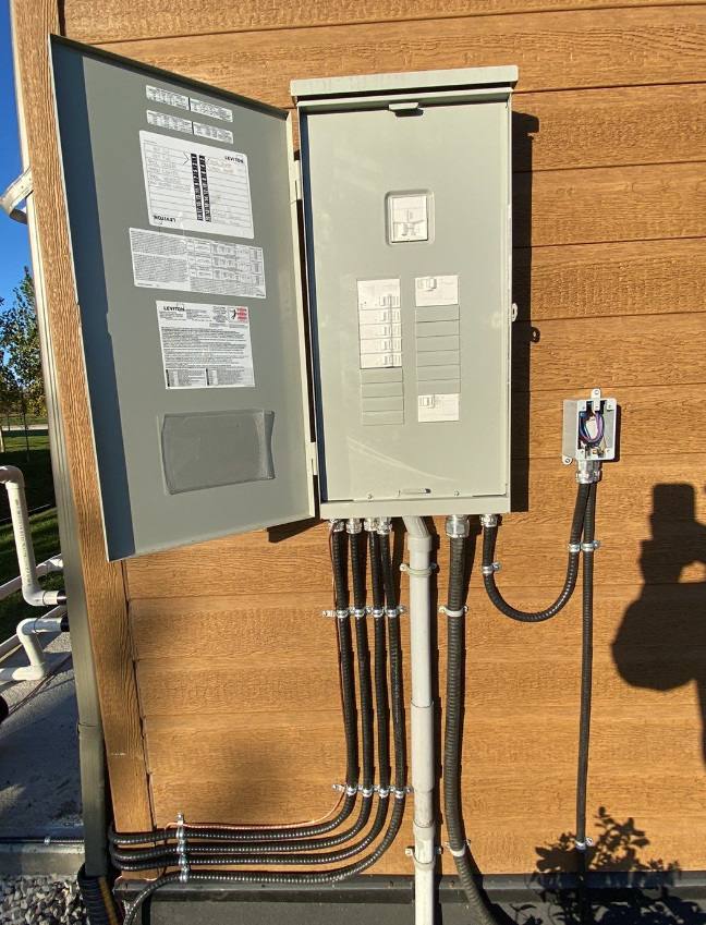 Outdoor electrical panel with its door open and several neatly strapped conduit runs leaving the bottom